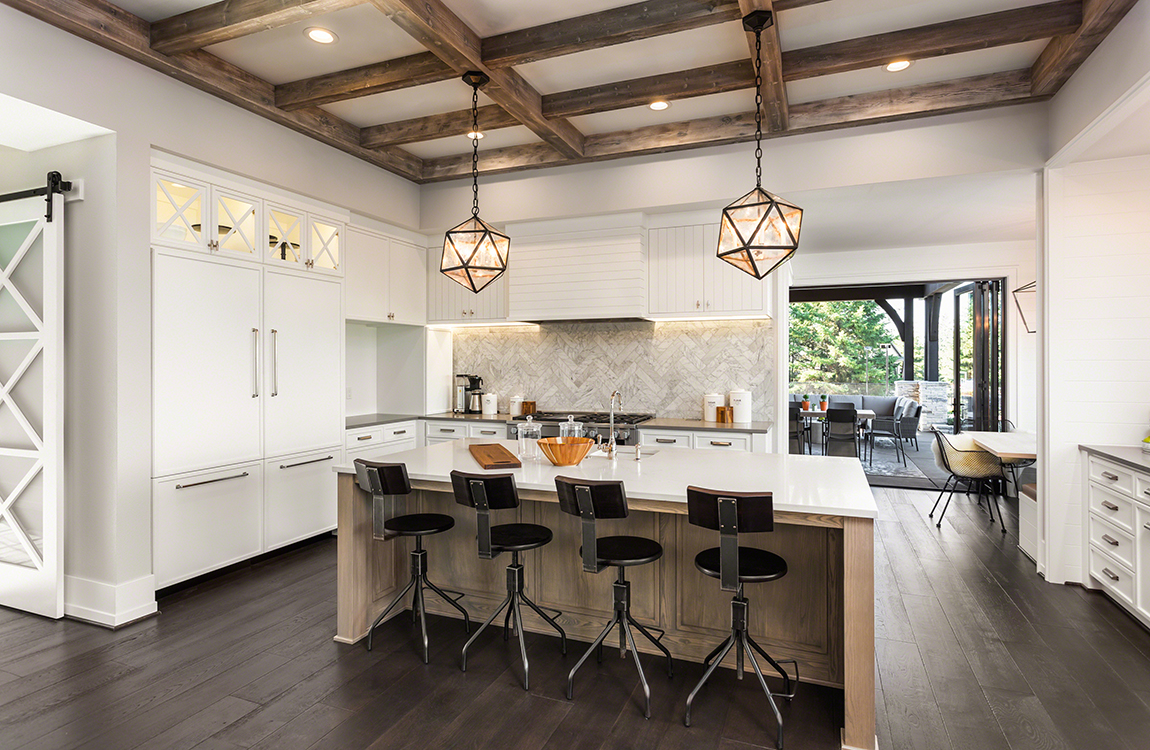 Kitchen Interior with Island, Sink, Cabinets, and Hardwood Floors in New Luxury Home. Includes elegant pendant light fixtures and wood beam ceiling